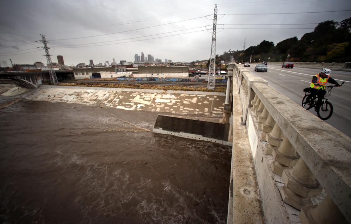 A man rides his bike across the Buena Vista Street Bridge as a swollen Los Angeles River flows below in Lincoln Heights in January. County officials are looking into ways to fund projects to capture more stormwater.
