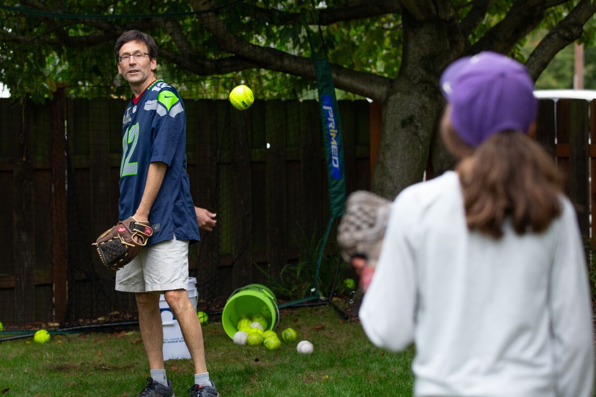 Bob Ferguson and his daughter Katie, 11, practice behind-the-back pitching at their Seattle home. 