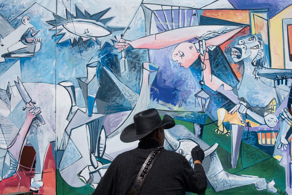 A man dressed in black, with black gloves, works on a Cubist painting 