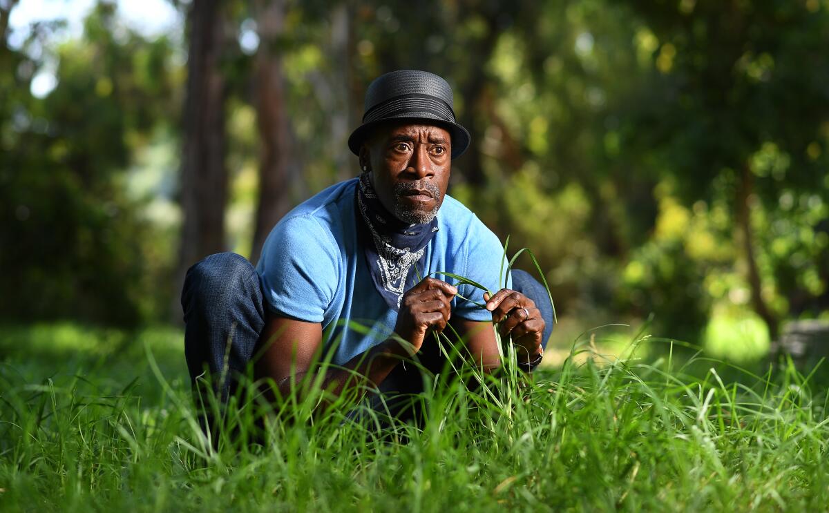 A Black man in a hat crouches down in grass