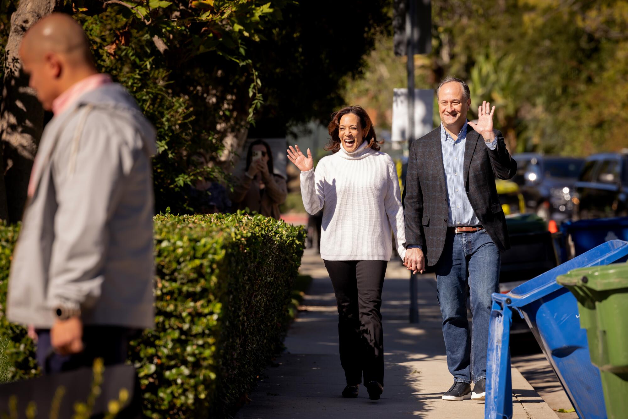 Vice President Kamala Harris and Second Gentleman Doug Emhoff wave and walk down a sidewalk.