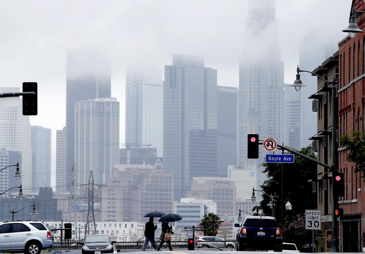 Pedestrians cross 1st Street in Boyle Heights as rain clouds partially obscure the downtown L.A. skyline during a storm in March.