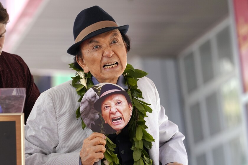 An actor holds up a paper fan with his own snarling face and growls playfully.