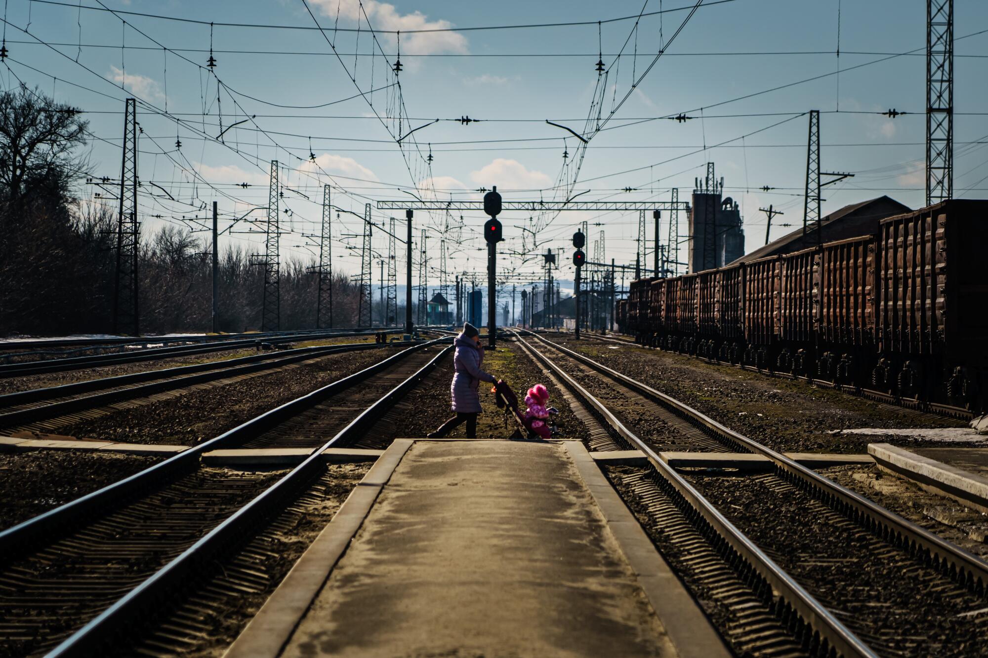 A woman pushes a baby in a stroller across railroad tracks at the train station in Kozacha Lopan, Ukraine