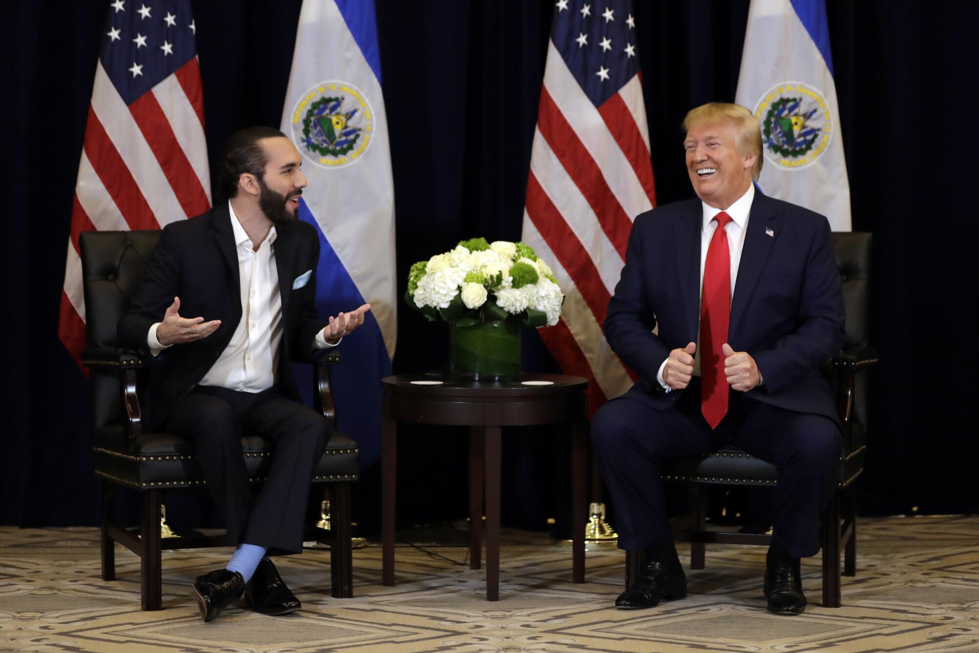 President Trump sits with President Nayib Bukele, both smiling, in front of flags.