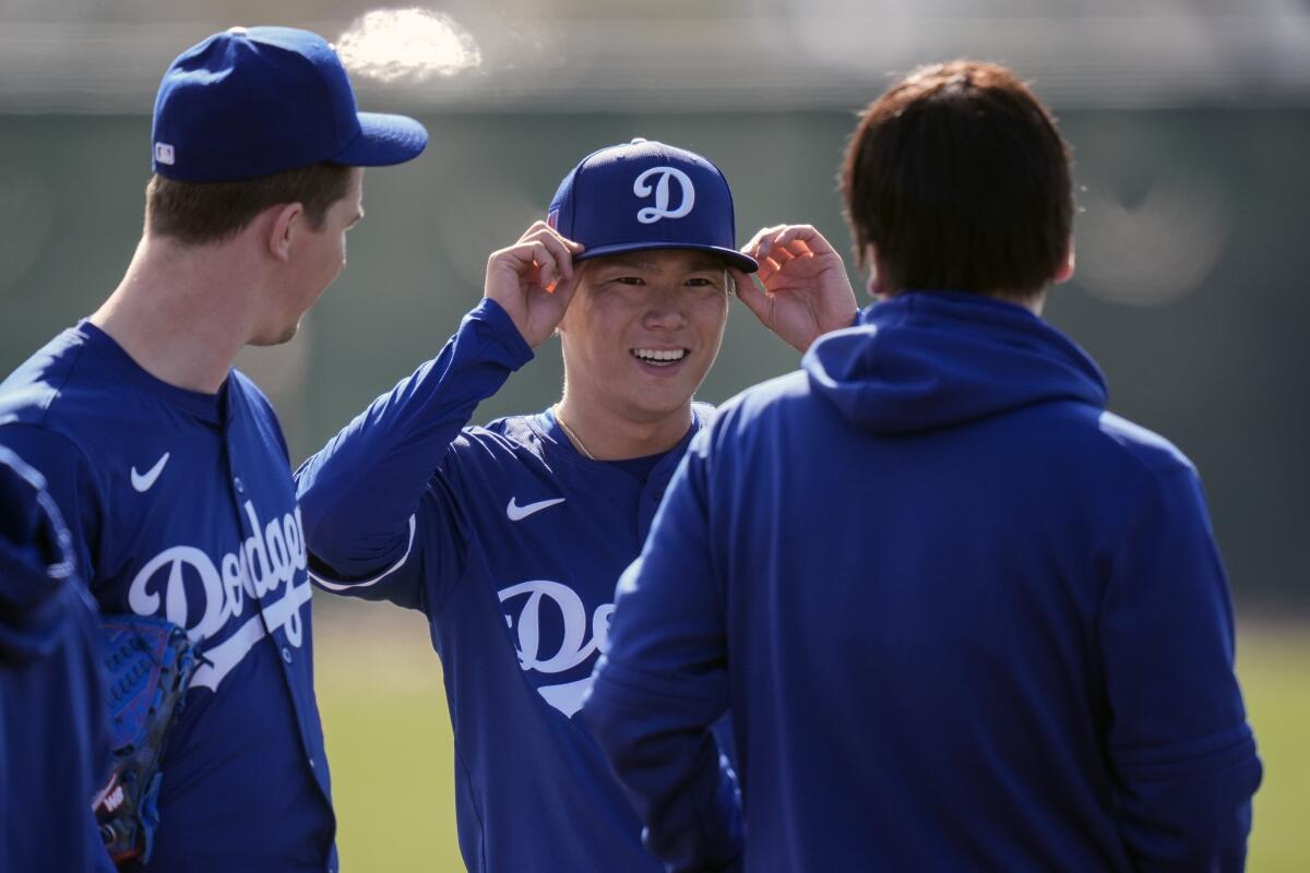 Dodgers pitcher Yoshinobu Yamamoto, center, adjusts his cap as he talks with teammates and staff on the field.
