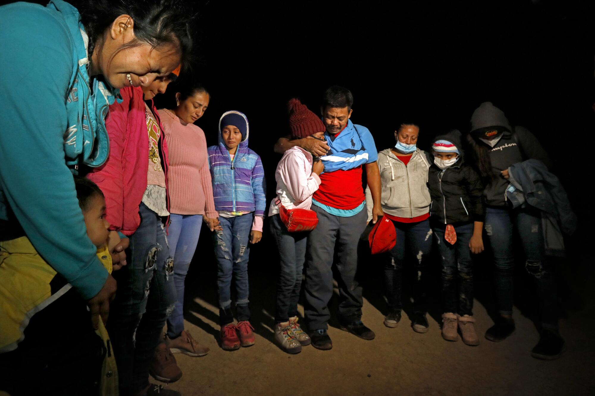 A group of migrants, some crying, stand together at night