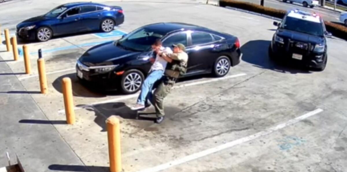 A deputy lifts a man off his feet from behind in a surveillance video image of a 7-Eleven parking lot