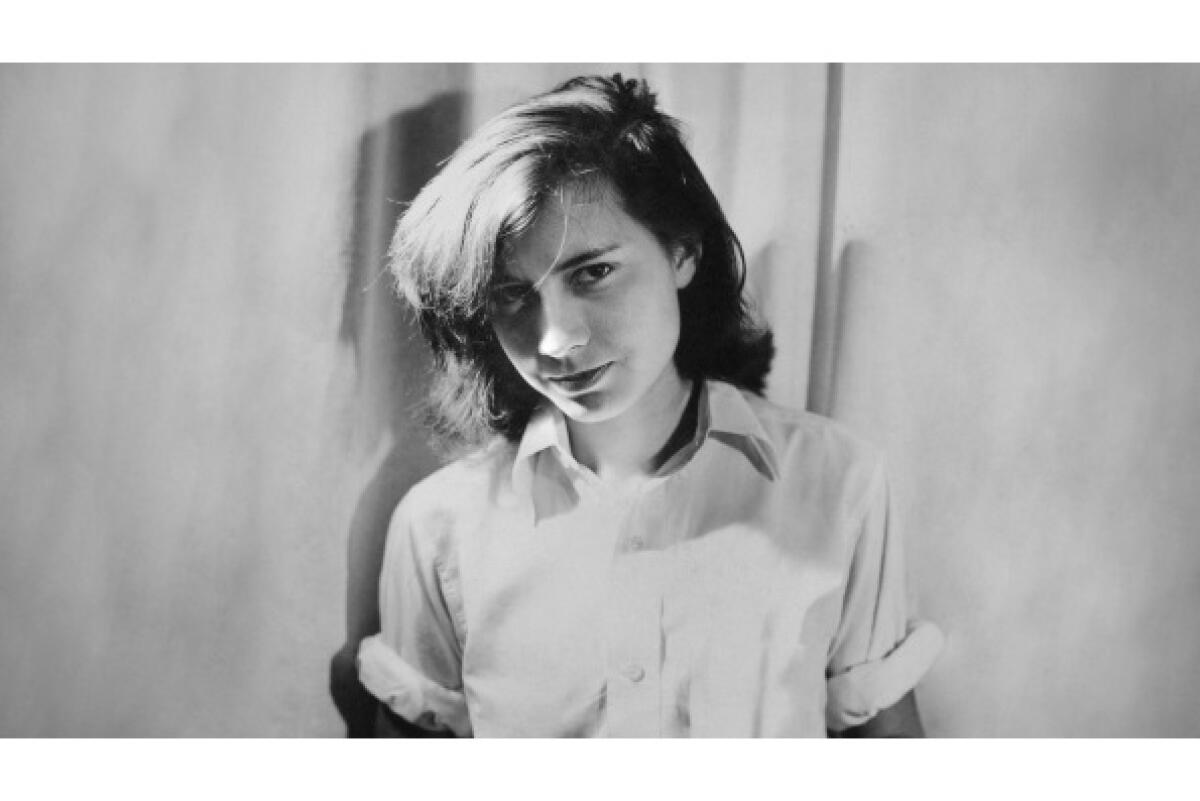 Close-up of a slightly smiling young woman in a white button-down shirt with the sleeves rolled above the elbow.