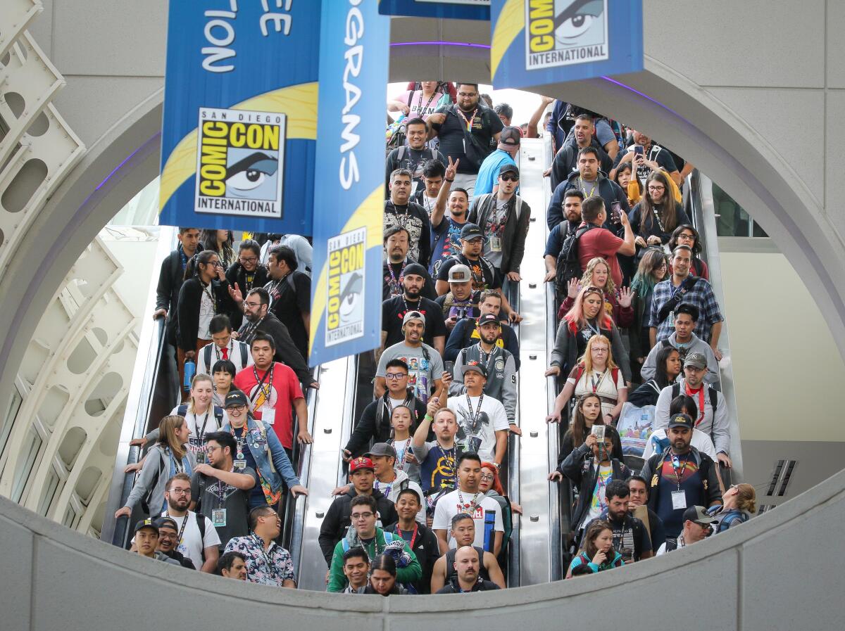 People ride down three parallel escalators underneath San Diego Comic-Con banners