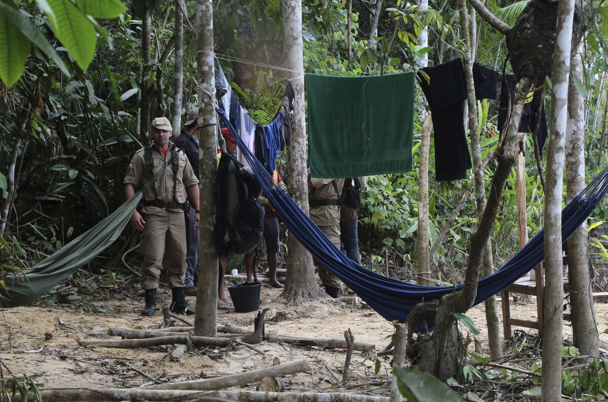 Man in khaki clothing stands amid hammocks and towels on clotheslines hanging from trees 