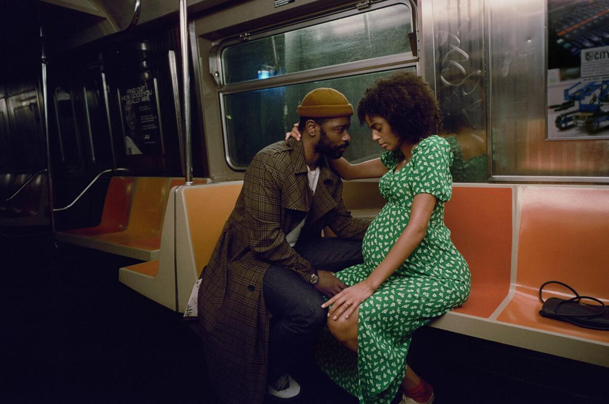 A man and a pregnant woman embrace while sitting in a subway car.
