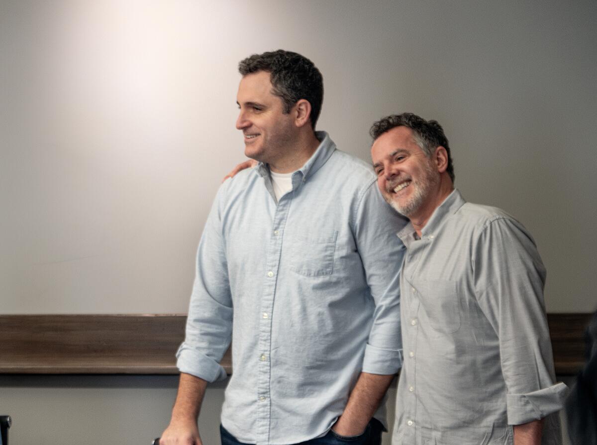 Joe Cristalli, in a blue button-up shirt, stands next to Chris Harris, who has his arm around him.