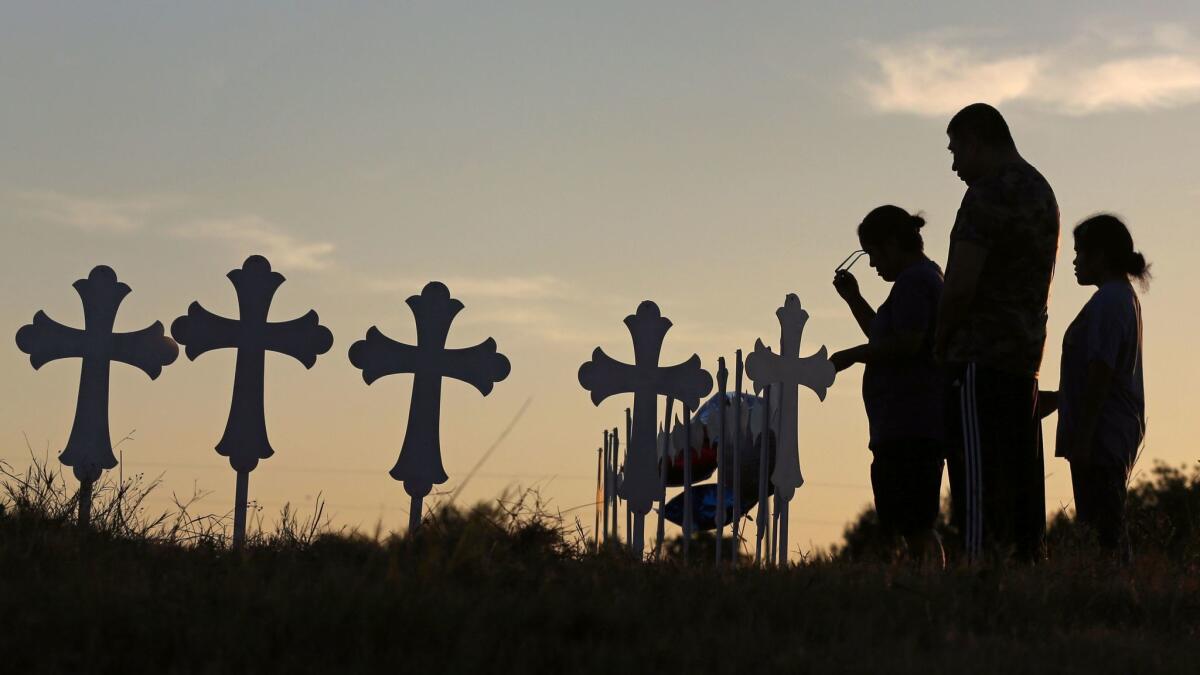 Irene and Kenneth Hernandez and their daughter Miranda Hernandez say a prayer Monday in front of crosses memorializing victims of the mass shooting in Sutherland Springs, Texas.