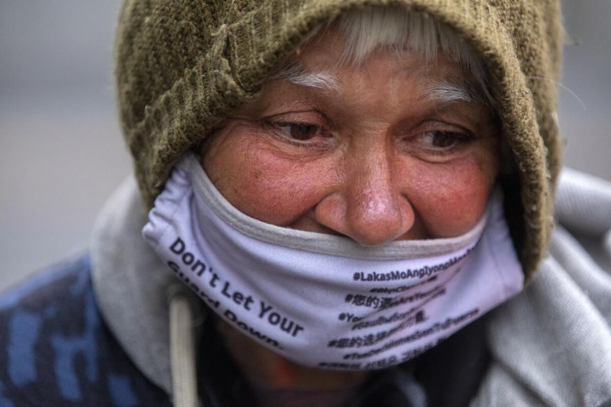 A closeup of a homeless woman in Los Angeles wearing a knit cap and lavender facemask. 