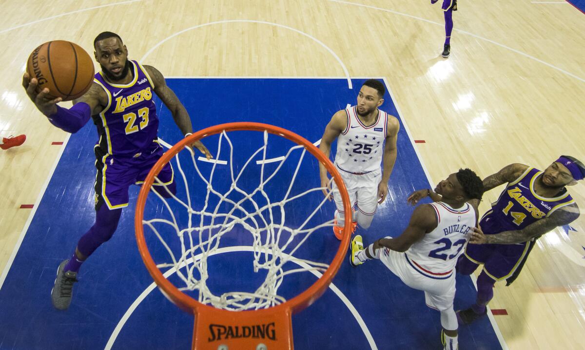 Los Angeles Lakers' LeBron James, left, goes up for the shot as Philadelphia 76ers' Ben Simmons, center, of Australia, and Jimmy Butler, right, look on during the second half of an NBA basketball game, Sunday, Feb. 10, 2019, in Philadelphia. The 76ers won 143-120.