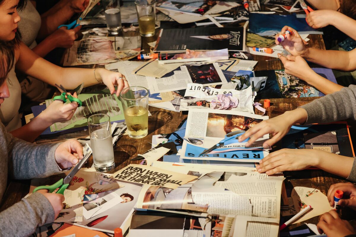 People sit at a table with magazines, glue and scissors at a collage meetup in Los Angeles.