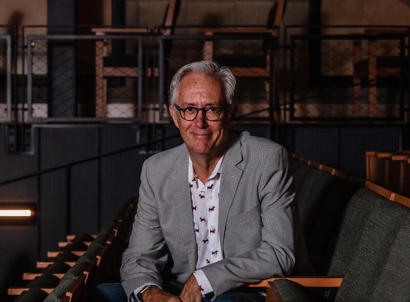 Sean Murray, in a gray blazer and jeans, sits on a dark gray chair in a theater.