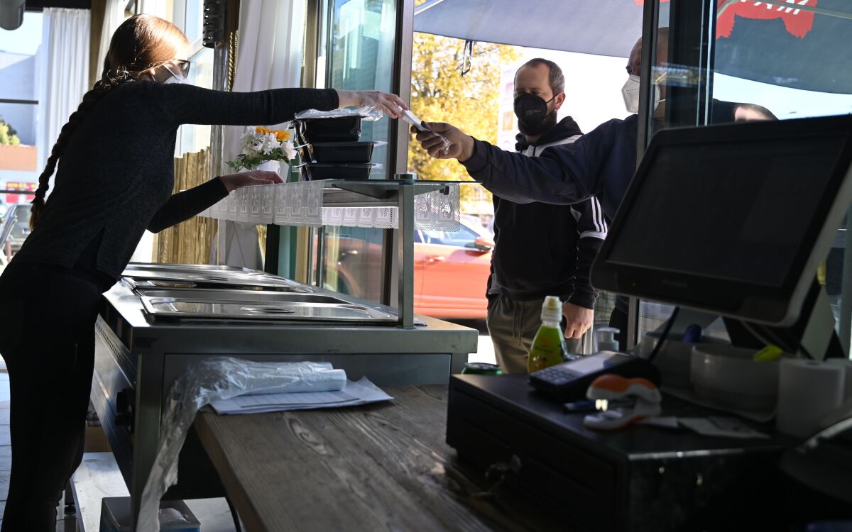 FILE - People wear face masks to curb the spread of COVID-19 at a restaurant which sells packed lunches from a window, in Michalovce, Slovakia, on Oct. 25, 2021. Slovakia is planning to gradually ease most coronavirus restrictions despite a current record surge of infections caused by the highly transmittable omicron variant. Prime Minister Eduard Heger says that people will have access to stores, shopping malls, various public gatherings and services, including bars and restaurants, without any restrictions. (Roman Hanc/TASR via AP, File)