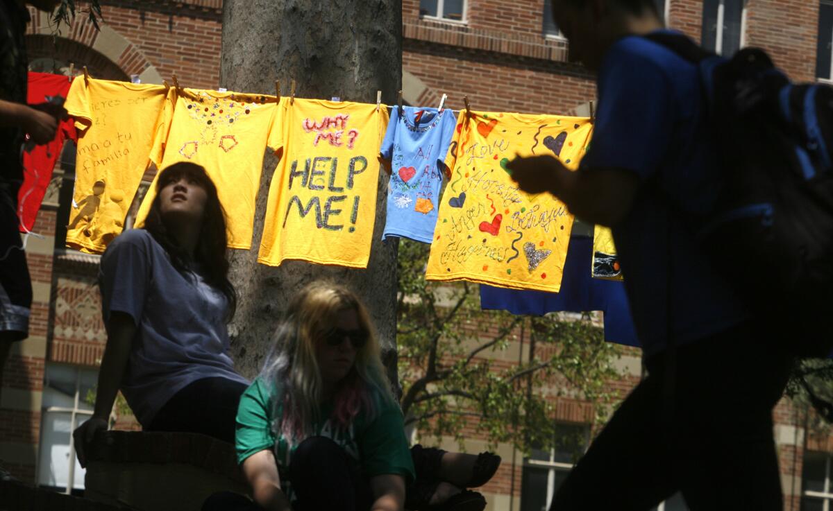 In the Clothesline Project at UCLA, survivors of domestic violence make yellow shirts to raise awareness of gender violence. Courtney Kiehl, left, sits near the line of shirts as other students pass by the display in 2011.