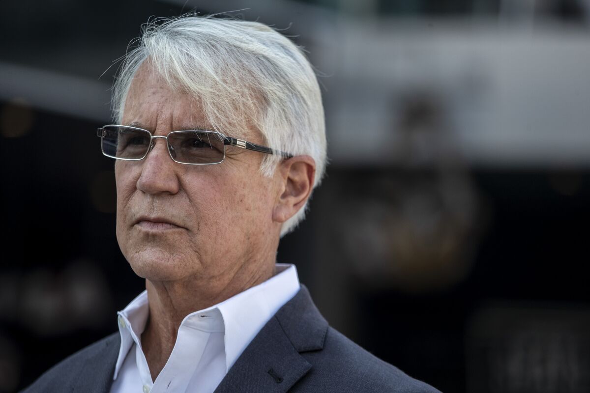 A man with an open collar shirt and suit jacket, silver hair and sunglasses.