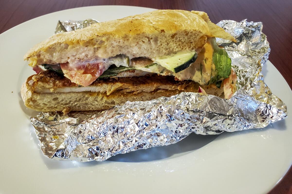 Air-fried chicken sandwich on toasted ciabatta sits on foil on a white plate