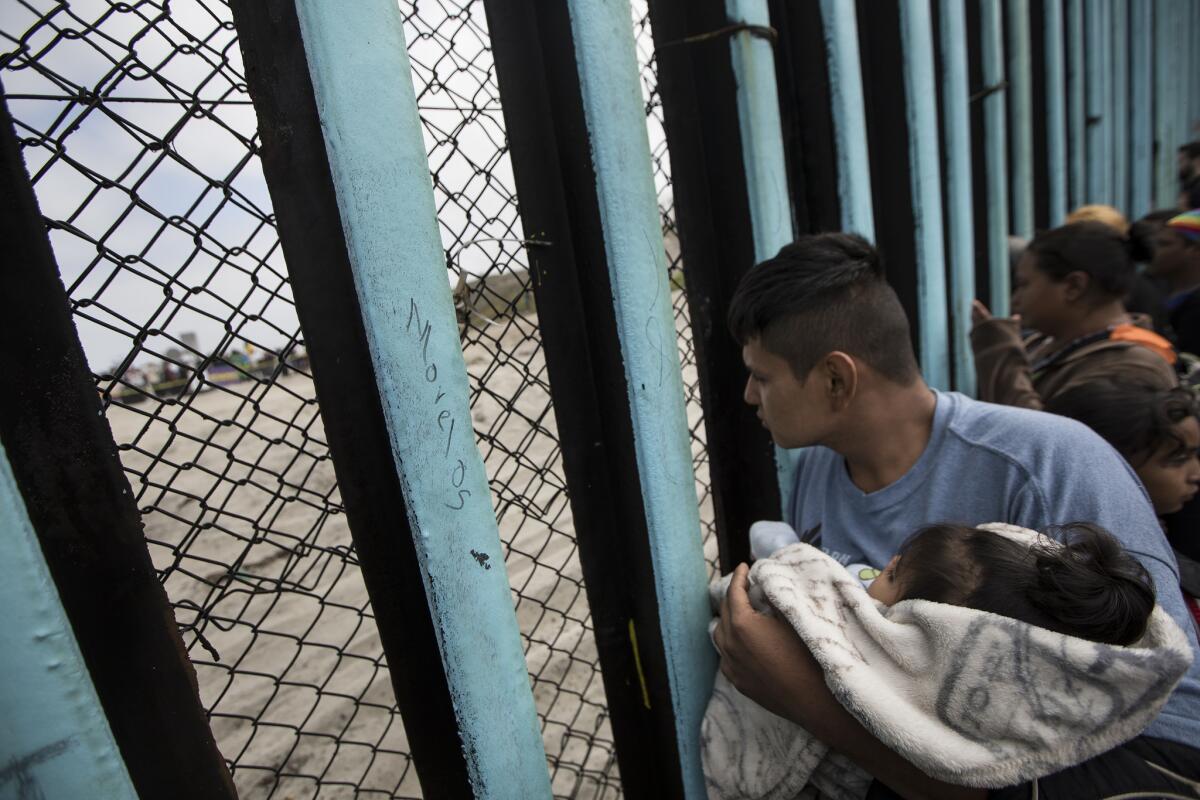 A member of the Central American migrant caravan, holding a child, looks through the border wall in Tijuana in April.