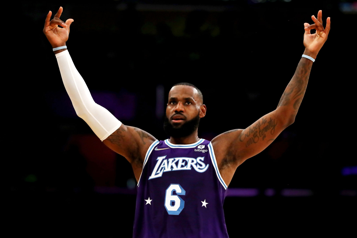 A bearded man, in a purple basketball jersey with the word Lakers and the number 6, raises his arms 