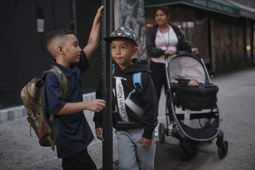 Kimberly Carchipulla, right, and her son 5-year-old Damien, center, wait for the bus on their way to school on Thursday, Sept. 7, 2023, in New York. Damien attends his first day of school in New York City after his family emigrated from Ecuador in June. Carchipulla and her family have been living in a room at the historic Roosevelt Hotel, converted into a city-run shelter for newly arrived migrant families hoping to find work, a new home and a better life for their children. (AP Photo/Andres Kudacki)