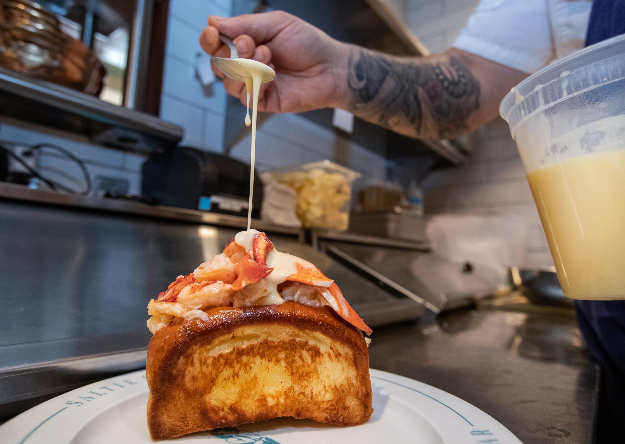 Chef Kyle McClelland spoons on beurre blanc sauce while preparing a warm lobster roll at Saltie Girl.