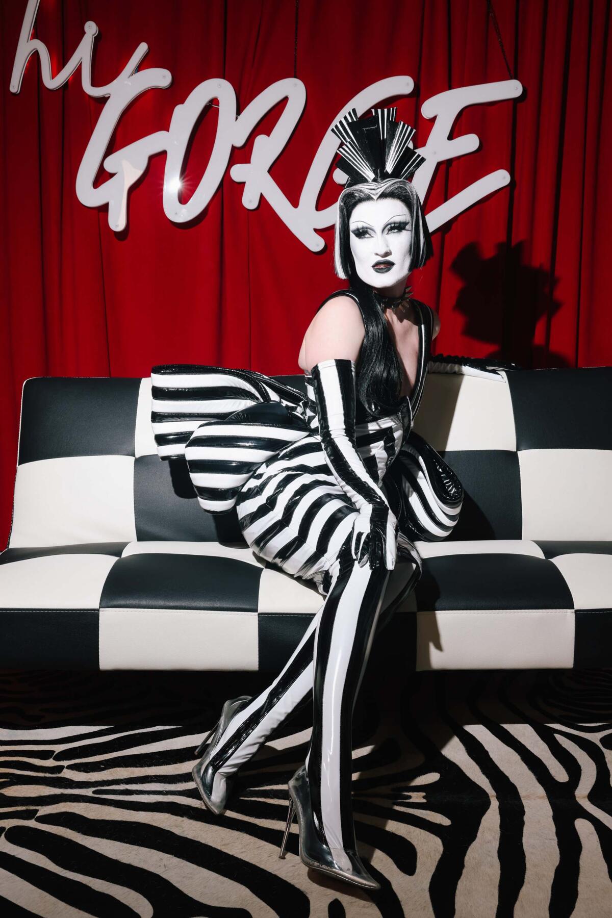 A person in a black-and-white striped dress sits on a checkered sofa on top of a zebra print rug.