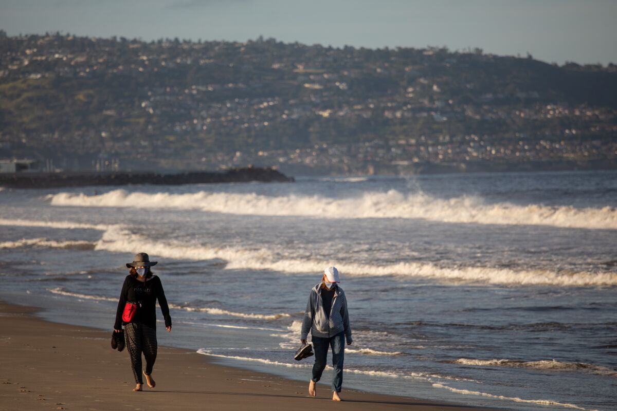 People wearing masks walk along Hermosa Beach.