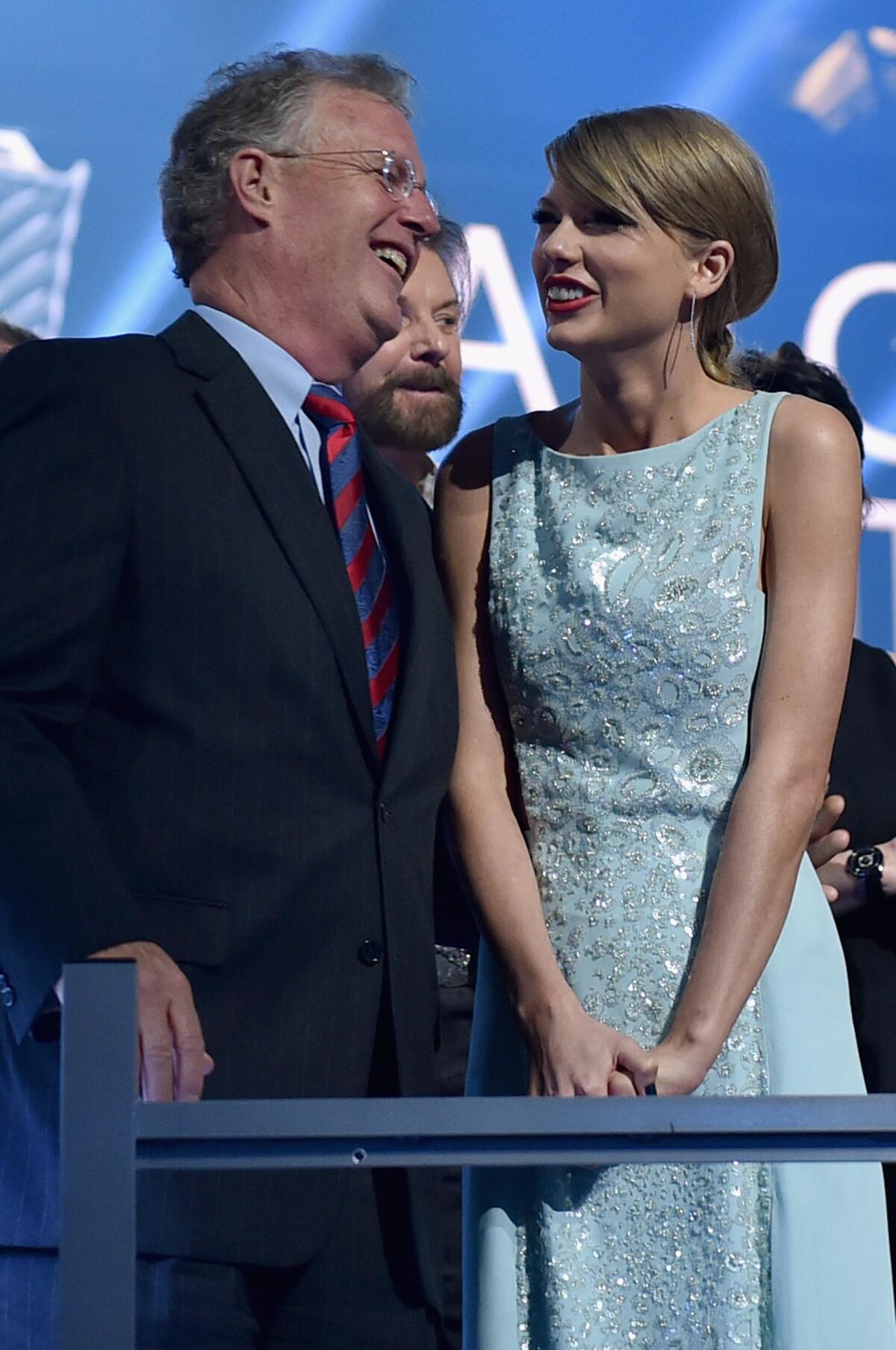 Scott Swift and his daughter Taylor Swift wear formalwear while smiling at each other behind a railing