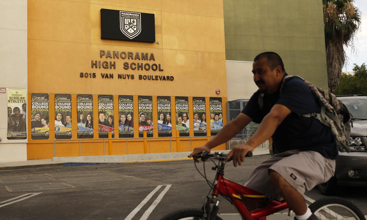 A  man rides a bike in front of Panorama High School