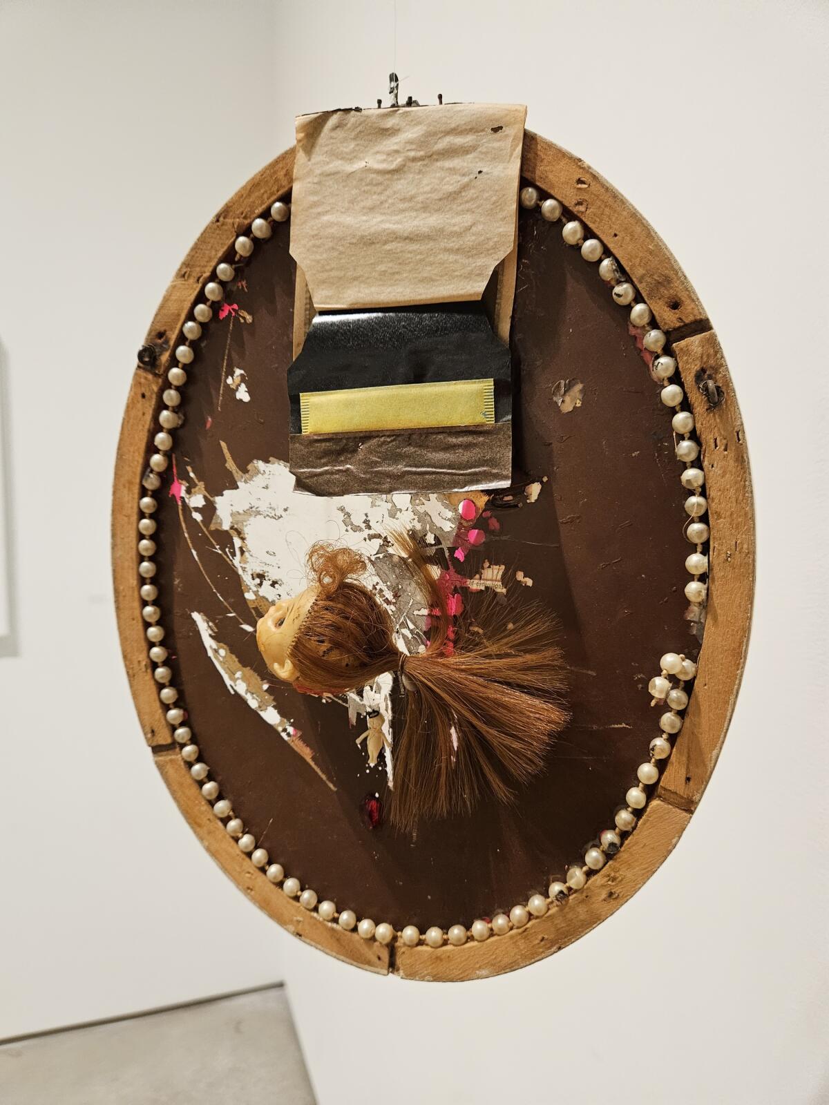 An oval panel framed by a string of pearls with the severed head of a doll.