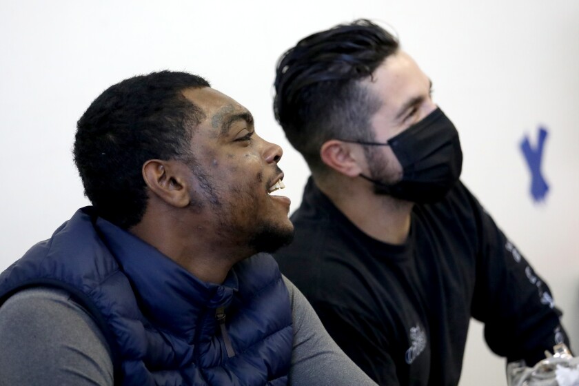 Two men, the one on the right wearing a face mask, sit smiling