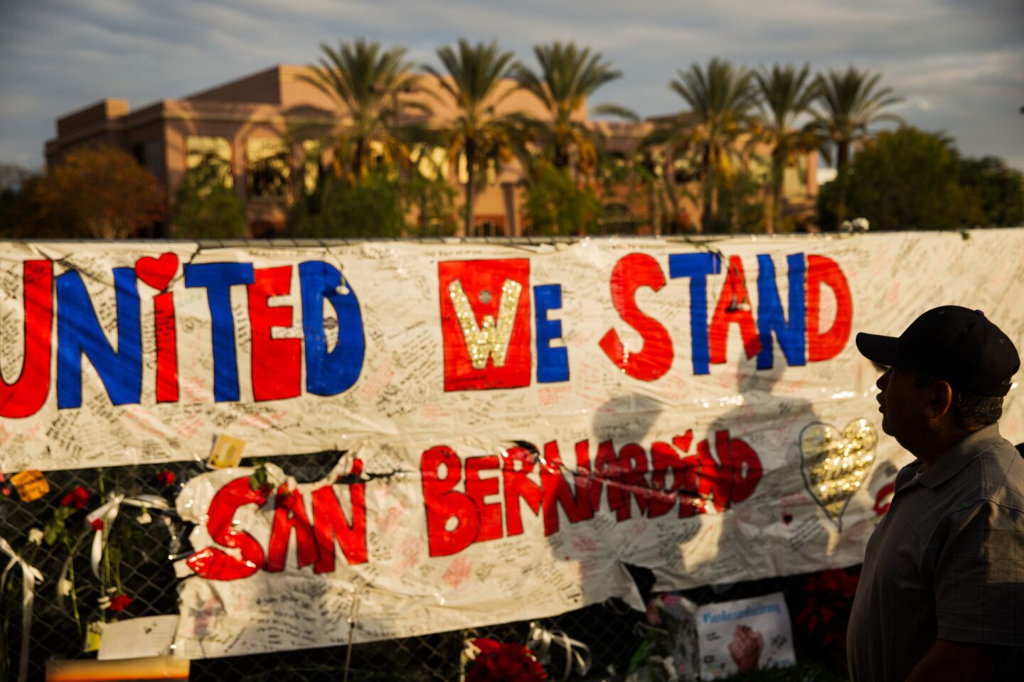 Visitors arrive to pay their respects at the makeshift memorial outside the fenced off Inland Regional Center, in the background, the site of the deadly terrorist attacks, in San Bernardino, Calif.