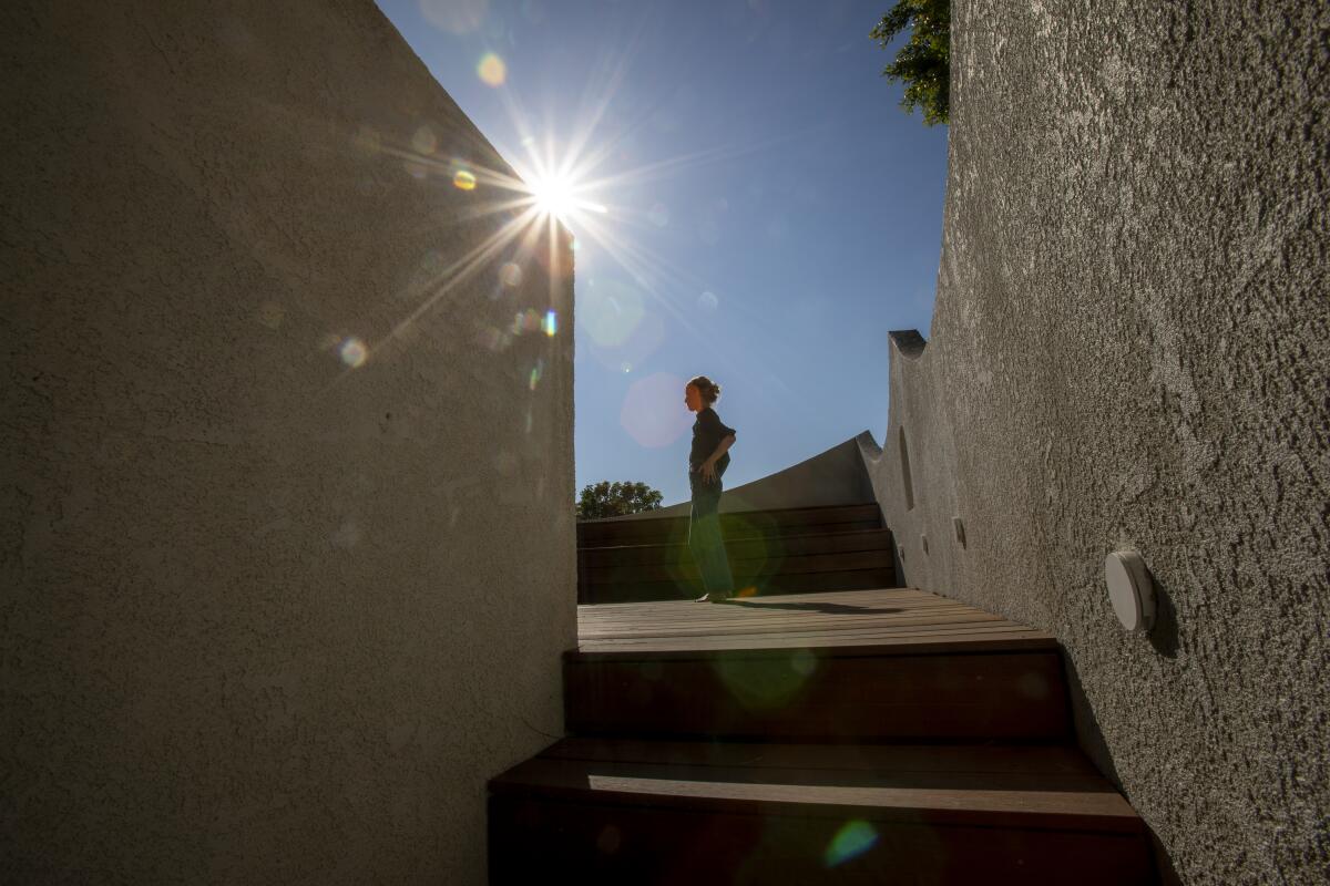 A woman stands at the top of a stairway, silhouetted against the sun