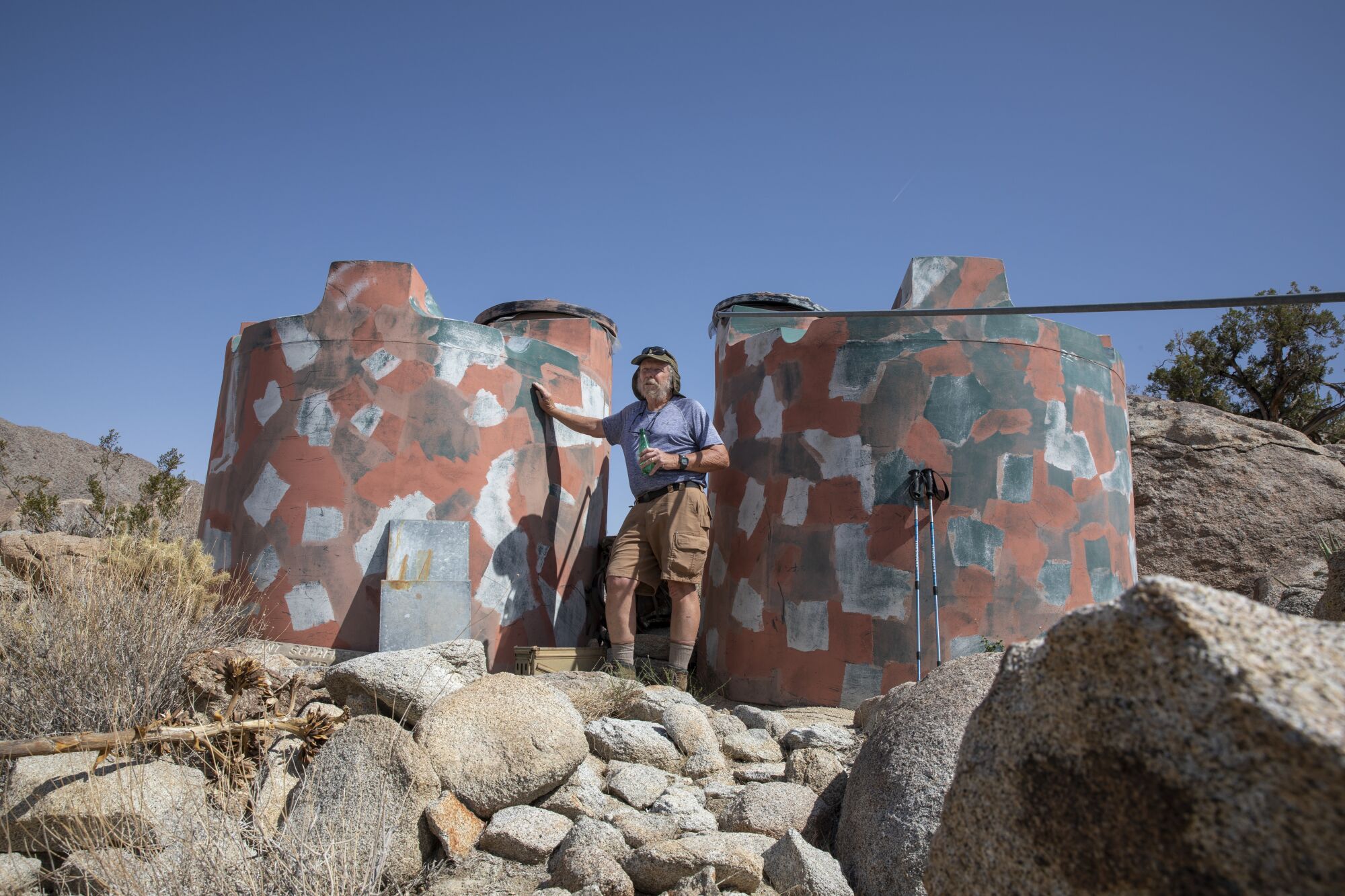 Mark Jorgensen stands by two water tanks in the desert.