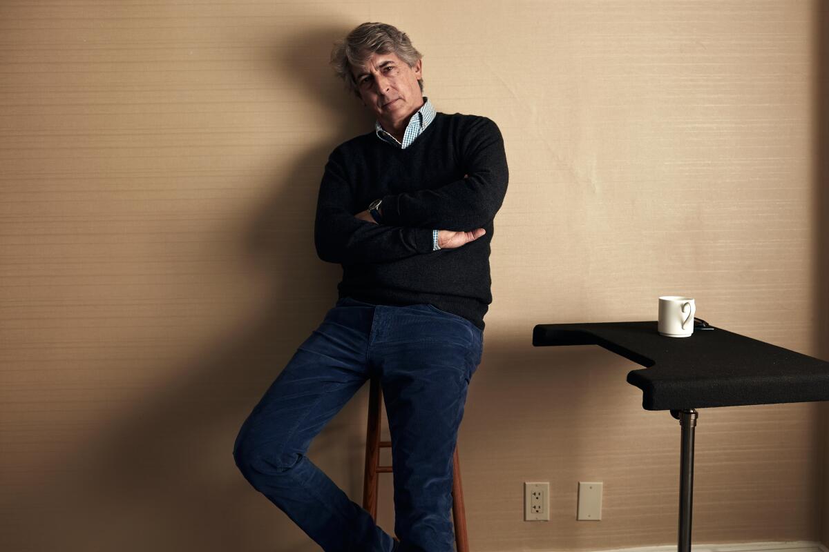 Alexander Payne crosses his arms and sits on a stool for a portrait.