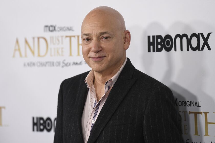 Evan Handler smiles in a black pinstripe suit and pink collared shirt.