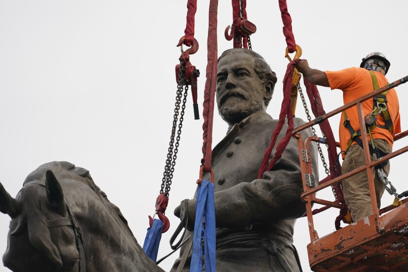 A worker in a hard hat stands on a lift alongside a statue of a man on a horse surrounded by cables and chains.