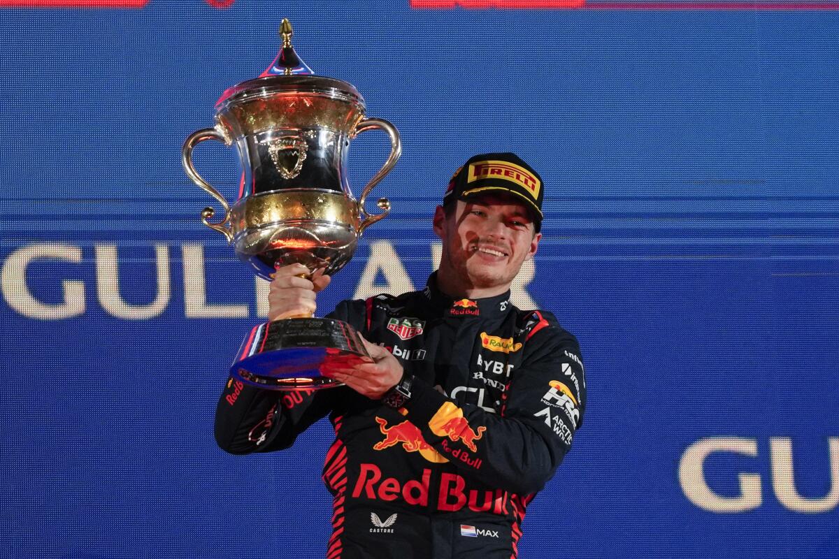 Red Bull driver Max Verstappen holds up a large trophy and smiles.