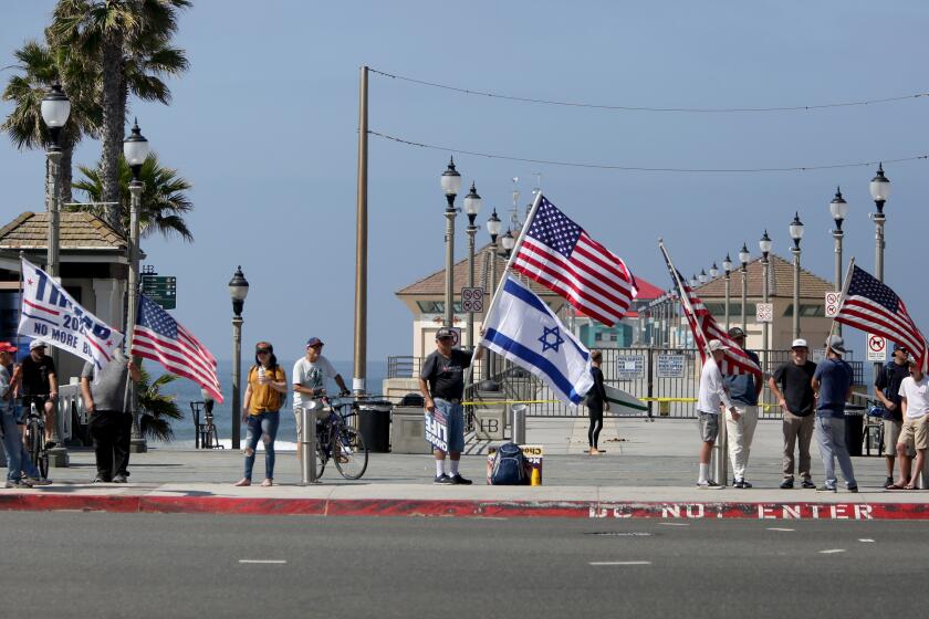 Some protesters hold flags and signs up at the entrance to the pier in Huntington Beach on Saturday.