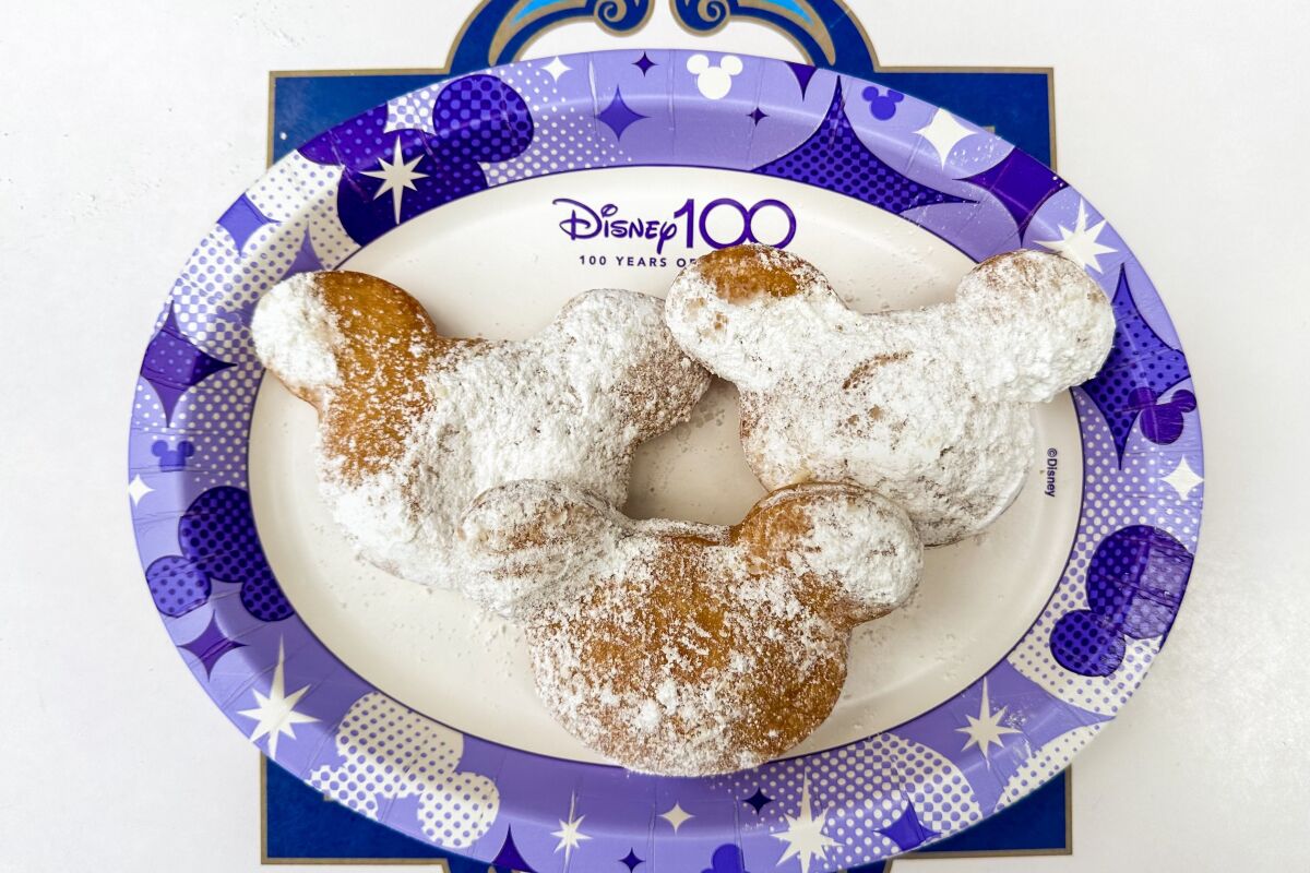 Mickey Mouse-shaped beignets on a blue-and-white paper plate marked "Disney 100"