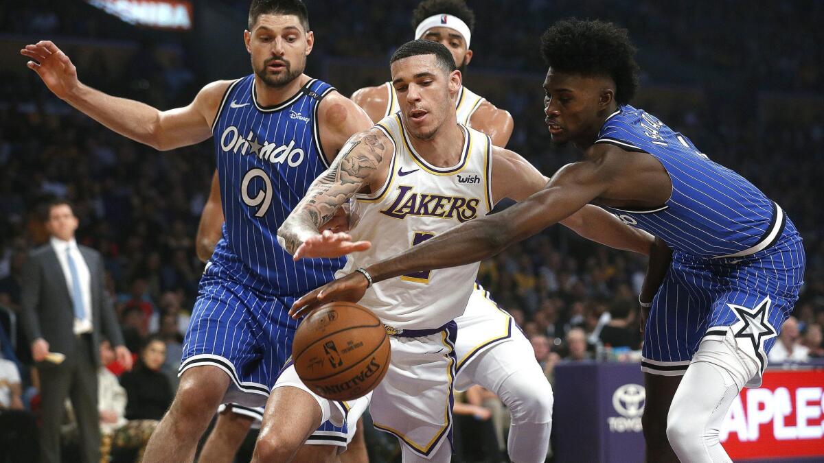 Lakers guard Lonzo Ball fights for a loose ball with Orlando Magic center Nikola Vucevic (9) and forward Jonathan Isaac at Staples Center on Sunday.