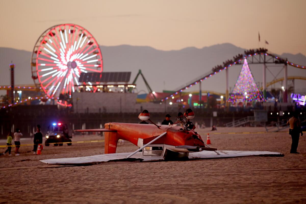 A single-engine Cessna airplane upside down on the beach in front of a pier with rides on it