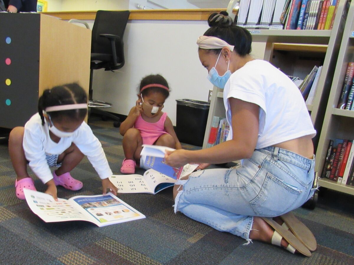 Trang Huynh (right) looks over children's books at the La Mesa library with Analise Hofisi (left) and Juliana Hofisi.