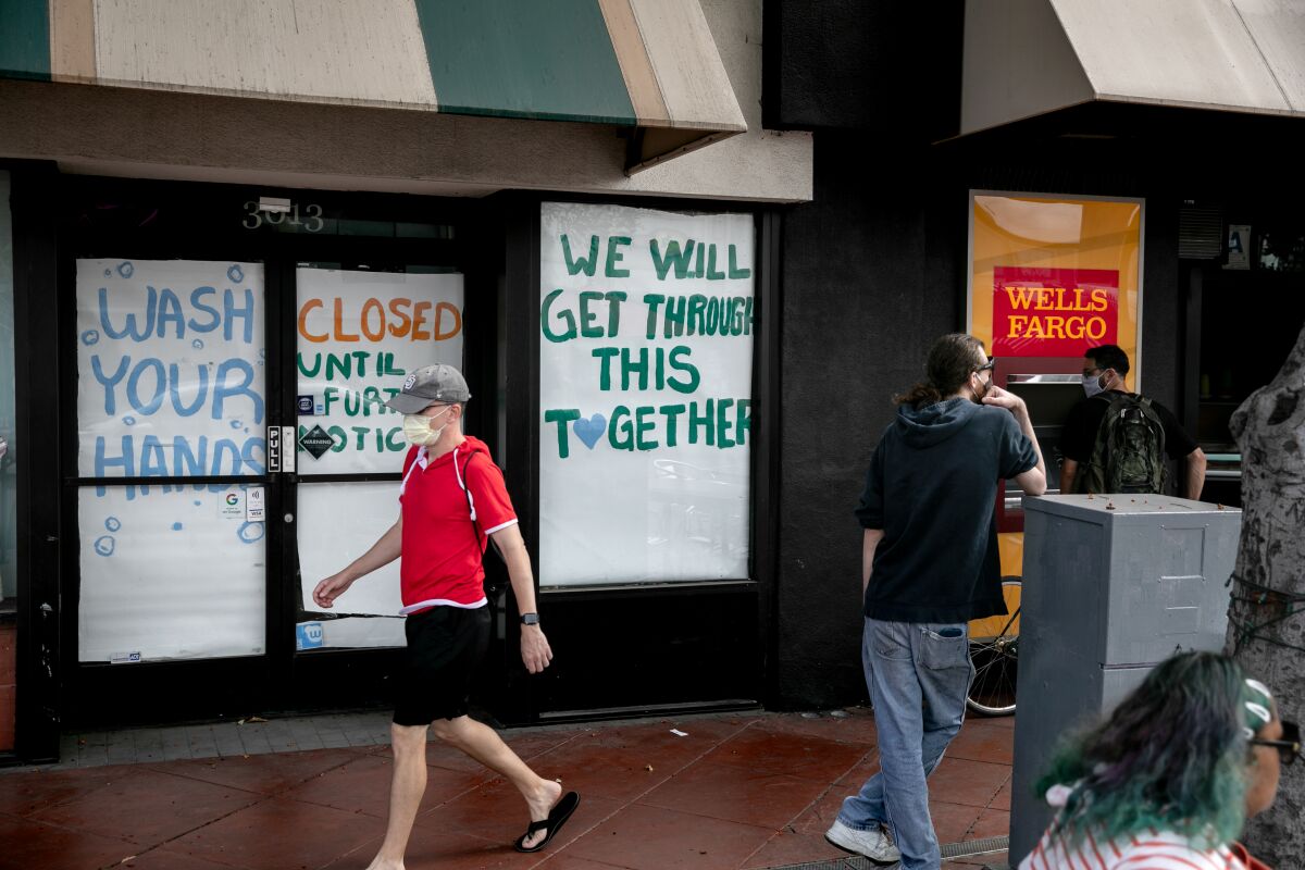 A man walks past a closed business with words of encouragement in the window.