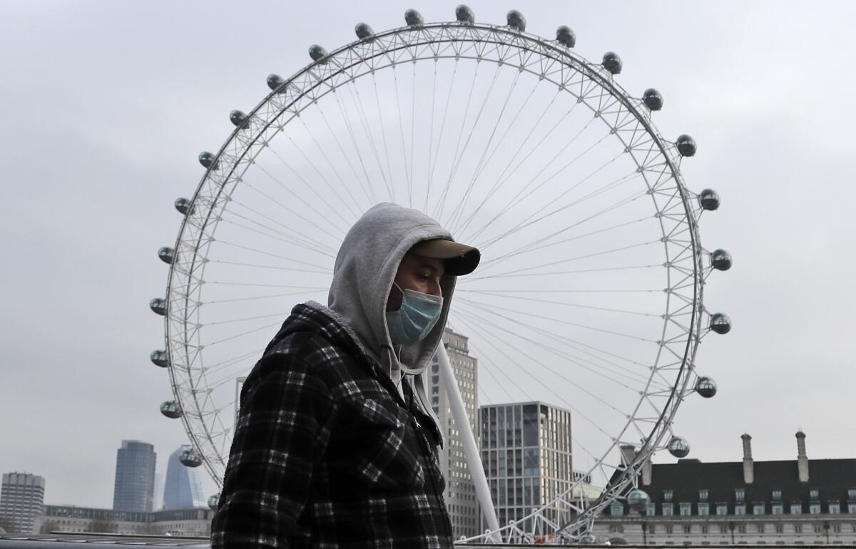 A man wearing a face covering walks past the London Eye in London